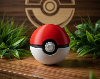 Puede incluir: Una Poké Ball roja, blanca y negra descansa sobre una superficie de madera, con un logotipo de Pokémon de madera en el fondo. Plantas y hierba verdes rodean la bola, creando una escena vibrante. La bola es un diseño clásico de la franquicia.