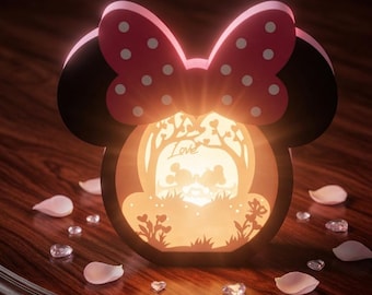 May include: A decorative lamp shaped like a mouse head with a pink polka-dot bow. The center features a backlit cutout scene of two figures kissing under a tree with the word Love written in script. The lamp emits a warm glow from within.