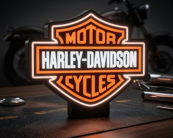 May include: A shield-shaped Harley-Davidson Motor Cycles sign with illuminated orange borders and white lettering. The sign features the iconic bar and shield logo with the text MOTOR, HARLEY-DAVIDSON, and CYCLES clearly displayed in a bold font.