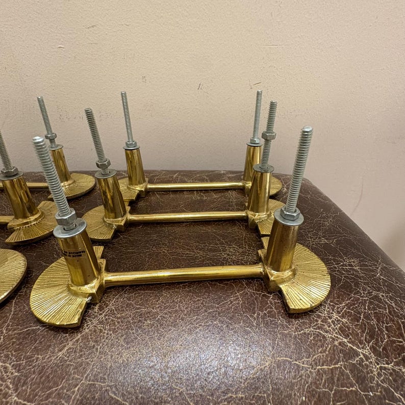 May include: A collection of brass cabinet pulls with a gold finish. Each pull features a decorative, fan-shaped base and a horizontal bar. The pulls have threaded rods for installation, with nuts and washers.