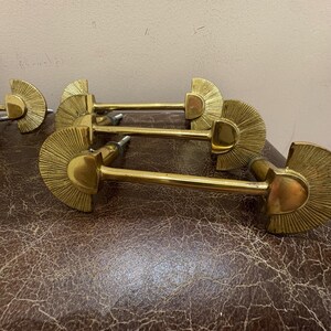 May include: A set of brass cabinet pulls. Each pull features a fan-shaped design with a central, rounded element and a long, straight handle. The pulls are a bright gold color and appear to be vintage.
