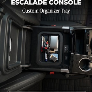 Op de afbeelding: Zwarte op maat gemaakte organizerlade voor een Cadillac Escalade-console. De lade is open en onthult compartimenten met sleutels, pennen en andere kleine items. De tekst luidt "TRANSFORM YOUR ESCALADE CONSOLE Custom Organizer Tray."