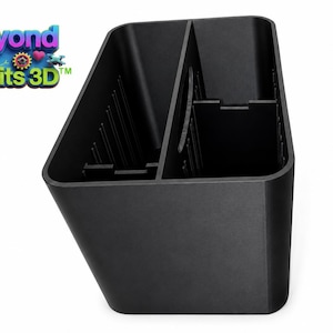 May include: A black plastic storage organizer with a rectangular shape and a central divider. The interior features vertical ribbed slots along the sides for adjustable partitioning. The logo Beyond Limits 3D is visible in the upper left corner.