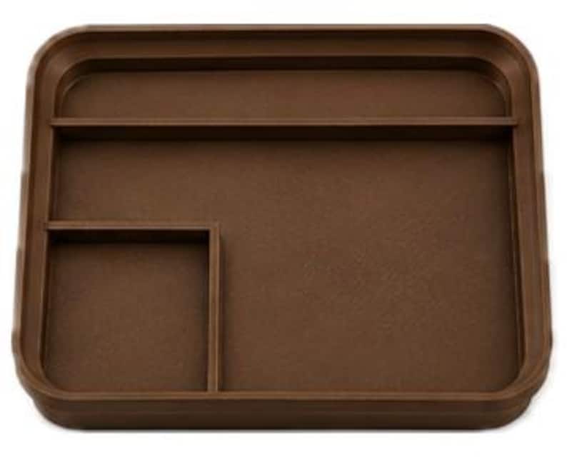 Op de afbeelding: Een bruine rechthoekige tray met afgeronde hoeken en opstaande randen. De tray heeft twee interne compartimenten: een lange, smalle sectie en een kleinere vierkante sectie, ideaal voor het organiseren van kleine items.