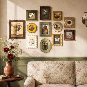 May include: A gallery wall arrangement featuring eleven diverse picture frames in various shapes, colors, and textures, including scalloped, beaded, and smooth edges. The frames display botanical prints, portraits, and nature scenes on a beige wall.