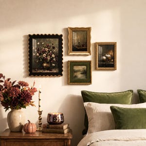 Pode incluir: Uma coleção de quatro quadros de parede com naturezas-mortas, um vaso de cerâmica com arranjos florais escuros, uma vela alta num suporte dourado, uma pequena abóbora e um castiçal de vidro sobre uma mesa de cabeceira de madeira.