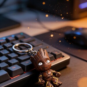 May include: A brown Groot keyring with a silver ring. The Groot figure has a detailed wooden texture, white eyes, and yellow accents. It is placed on a black keyboard and mousepad, with a blurred background.