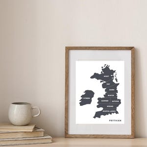 May include: A framed print with a map of Prythian, featuring labeled regions like Night, Day, Dawn, Winter, Summer, Autumn, Spring, Mortal Lands, and Hybern. The map is in dark gray against a white background, set in a wooden frame.