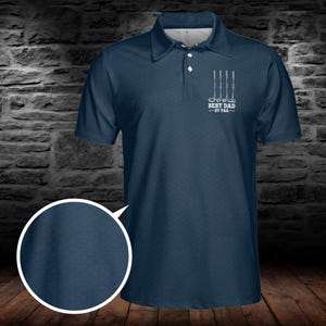 Op de afbeelding: Marineblauwe poloshirt met een textuurpatroon. Het shirt heeft een witte afbeelding van golfclubs en de tekst "BEST DAD - BY PAR". Het heeft een kraag en een knoopsluiting.