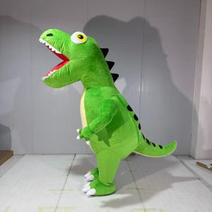 May include: A bright green plush dinosaur costume featuring a large head with an open mouth, white teeth, and a red interior. The creature has a pale yellow belly, black spikes along its back and tail, and white claws on its feet and hands.
