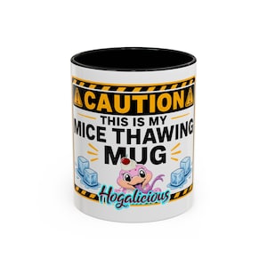 May include: White ceramic mug with a black interior, featuring the text "CAUTION THIS IS MY MICE THAWING MUG" in black and yellow. A cartoon frog with a cherry on its head is also featured. The word "Hogalicious" is written in teal.