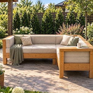 May include: An L-shaped outdoor sectional sofa constructed from light-toned wood with thick, beige upholstered cushions. The sofa features a matching beige seat and backrest, accented by two sage green throw pillows and one patterned beige pillow.