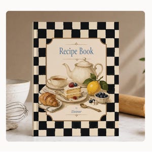 May include: A hardback recipe book featuring a black and white chequered border. The cover displays a cream-coloured centre with the text "Recipe Book" and "by Eleanor" above and below an illustration of a teapot, a teacup, a slice of cake, a lemon, and berries.