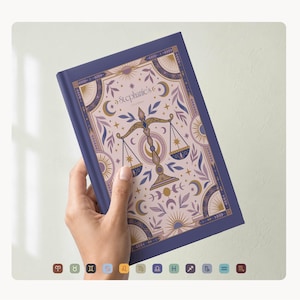 May include: A hardcover journal with a Libra zodiac design. The cover is a deep blue with a decorative illustration featuring scales, moons, and stars in shades of purple, gold, and pink. The text "Stephanie's Journal" is visible.