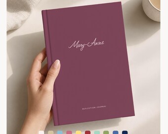 Puede incluir: Un diario de color burdeos con el nombre "Mary-Anne" en escritura cursiva. Las palabras "REFLECTION JOURNAL" están impresas en la parte inferior. El diario está sostenido por una mano. Una paleta de muestras de color está en la parte inferior.