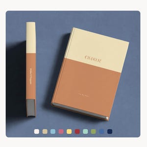 Op de afbeelding: Een minimalistische set van een notitieboek en pen. Het notitieboek is verdeeld in twee secties, met een beige bovenkant en een roestkleurige onderkant. De pen is roestkleurig met de tekst "Make It Happen". Het notitieboek heeft de naam "Charlie" erop.