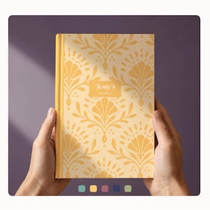 Könnte beinhalten: Ein Hardcover-Planer mit einem blassgelben Einband, der ein sich wiederholendes orangefarbenes florales Damastmuster aufweist. In der Mitte befindet sich ein rechteckiges Etikett mit dem weißen Text Jessy's PLANNER. Der Buchrücken ist einfarbig gelb.
