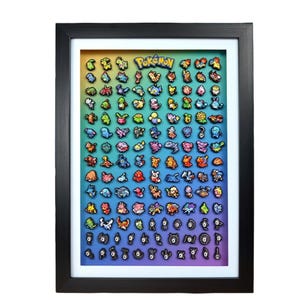 May include: Framed artwork featuring numerous colorful Pokémon characters arranged on a gradient background. The word "Pokémon" is displayed at the top. The artwork is encased in a black frame with a white border, creating a visually appealing display.