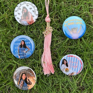 May include: A collection of personalized graduation buttons and a pink tassel with a gold charm. The buttons feature photos of a graduate, the text "Congrats," and the graduation year. The tassel is adorned with a gold charm that reads "2026."