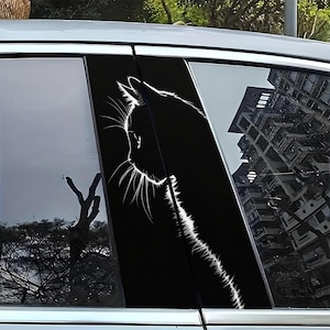 以下が含まれることがあります： 黒い車の窓用ステッカー。白い猫の横顔の輪郭が描かれています。猫のひげや顔の特徴が黒い背景に詳細に描かれています。ステッカーは車の窓に貼られています。