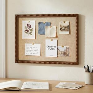 May include: A rectangular notice board with a dark brown beaded wooden frame and a tan linen-textured surface. It features several pinned items including a botanical print, fabric swatches, photographs, and a card with the text Creativity & Craft.