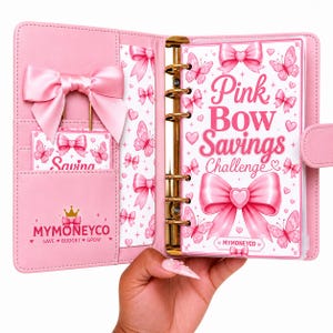 Pu&ograve; includere: Un raccoglitore rosa a sei anelli con un grande fiocco in raso sulla copertina sinistra e un inserto per la sfida di risparmio sulla destra. L'inserto mostra il testo Pink Bow Savings Challenge con grafiche di farfalle e fiocchi. Il marchio MYMONEYCO &egrave; visibile.