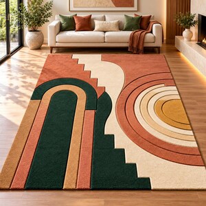 Könnte beinhalten: Ein rechteckiger Teppich mit einem geometrischen Muster in Dunkelgrün, gebranntem Orange, Hellbraun und Creme. Das Design umfasst geschichtete Bogenformen, konzentrische Kreise und treppenartige Kanten, die eine strukturierte Optik erzeugen.