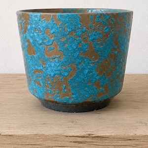 May include: A cylindrical ceramic planter featuring a textured, mottled finish with vibrant turquoise blue glaze layered over a dark brown base. The vessel has a wide, open top and a slightly tapered shape, showcasing a distinct contrast between the rough, raised blue surface and the smooth, dark brown clay body visible underneath.