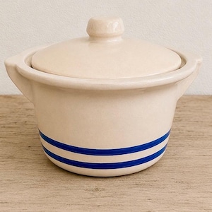 May include: A cream-colored ceramic casserole dish with a matching lid and two side handles. The exterior features two horizontal blue stripes encircling the lower portion of the pot. The surface has a smooth, glossy finish throughout the entire piece.