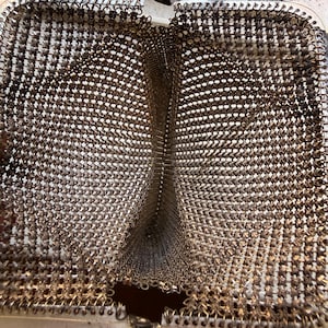 Op de afbeelding: Een open metalen mesh tas met een fijne, in elkaar grijpende zilverkleurige mali&euml;nkolderconstructie. Het interieur is verdeeld in twee afzonderlijke compartimenten door een centrale mesh scheidingswand, omlijst door een scharnierende metalen sluiting.