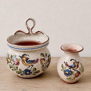 May include: A ceramic wall pocket with a top handle and a matching small vase, both featuring a cream-colored crackle glaze, hand-painted birds, and floral motifs in blue, yellow, and red tones with brown rim accents and terracotta interiors.