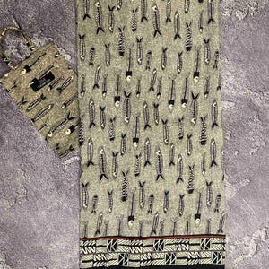 May include: A gray fabric with a repeating pattern of black and white fish skeletons. A matching tote bag is on the left. The fabric has a decorative border with geometric shapes and a red stripe.