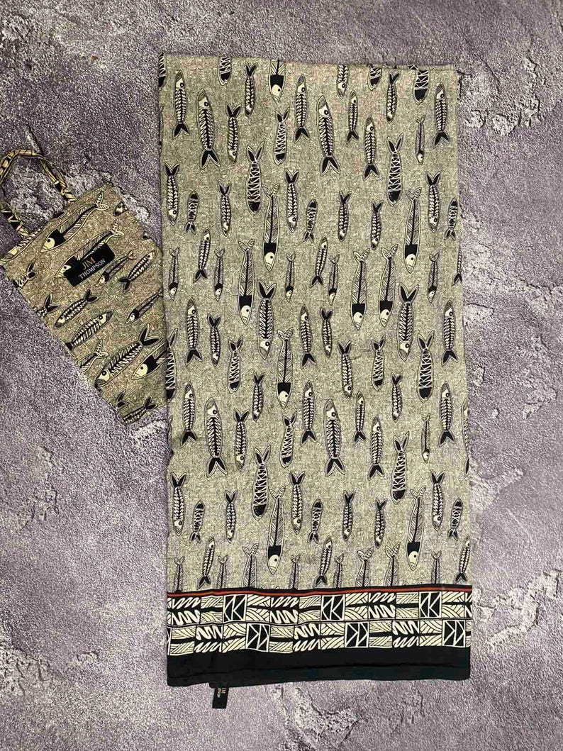 May include: A gray fabric with a repeating pattern of black and white fish skeletons. A matching tote bag is on the left. The fabric has a decorative border with geometric shapes and a red stripe.