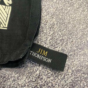 May include: Close-up of a black fabric with a white geometric design. A black tag with the gold text "JIM THOMPSON" is attached to the fabric. The fabric has a textured appearance.