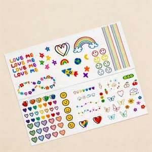 Op de afbeelding: Twee vellen kleurrijke stickers met verschillende ontwerpen. Het bovenste vel bevat de tekst "LOVE ME", een regenboog, sterren en smiley gezichten. Het onderste vel bevat harten, vlinders en bloemen.