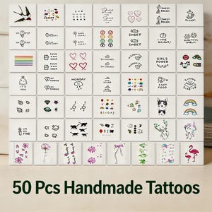 Könnte beinhalten: Eine Sammlung von 50 handgemachten temporären Tattoos. Die Designs umfassen einen Regenbogen, Herzen, Blumen, Tiere und Text. Der Text enthält Sätze wie "Sweet Dream" und "Good Luck!" Die Tattoos sind auf weißem Untergrund.