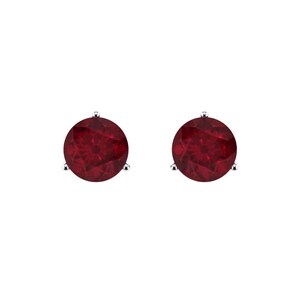Peut inclure: Une paire de boucles d'oreilles à clous avec des pierres précieuses rondes d'un rouge profond. Chaque pierre est fixée dans une monture en métal argenté à trois griffes, révélant une surface facettée qui reflète la lumière sur les faces circulaires.