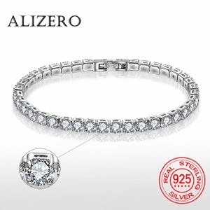 May include: A silver-toned tennis bracelet featuring a continuous row of round, clear, faceted stones set in metal links. The clasp is engraved with 925. A circular inset shows a magnified view of a single stone setting. The brand name ALIZERO is visible.