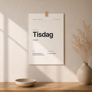 May include: A beige poster with the word "Tisdag" in large black font, along with the date "29 april". The poster is attached to a wall with a piece of tape. A vase with dried plants and a small bowl are in the foreground.