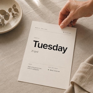 May include: A cream-coloured paper with the word "Tuesday" in bold black font. The date "29 April" is below. The paper includes the text "Walk in the park at 2 pm" and "Maria, home care". A hand holds the paper.