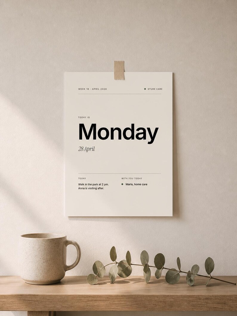 May include: A beige daily planner with the word "Monday" in large black font. The date "28 April" is below. The planner includes a to-do list and is taped to a wall. A beige mug and greenery are on a wooden surface.