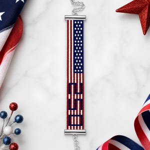 May include: A rectangular beaded bracelet featuring a red, white, and blue American flag pattern with the letters USA integrated into the design. The bracelet is finished with silver-toned metal end bars and a delicate silver-toned chain extender.