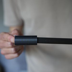 May include: A black metal rod with a cylindrical connector. The connector is a short, hollow cylinder that slides over the rod. The rod and connector are held by a person.