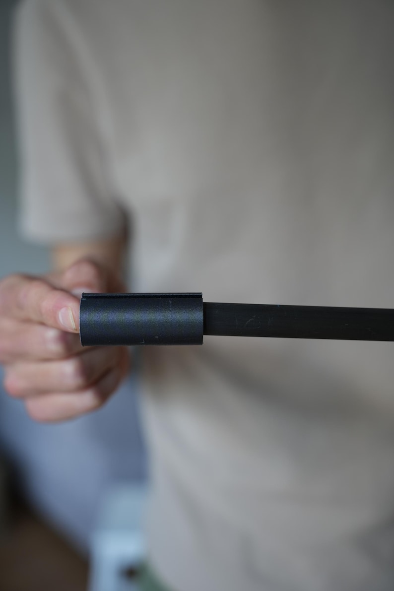 May include: A black metal rod with a cylindrical connector. The connector is a short, hollow cylinder that slides over the rod. The rod and connector are held by a person.
