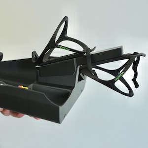 May include: Black plastic bicycle accessory with the word "VOXOM" in green. The accessory has a tray and two holders for water bottles. The holders are attached to the tray with a black elastic strap.