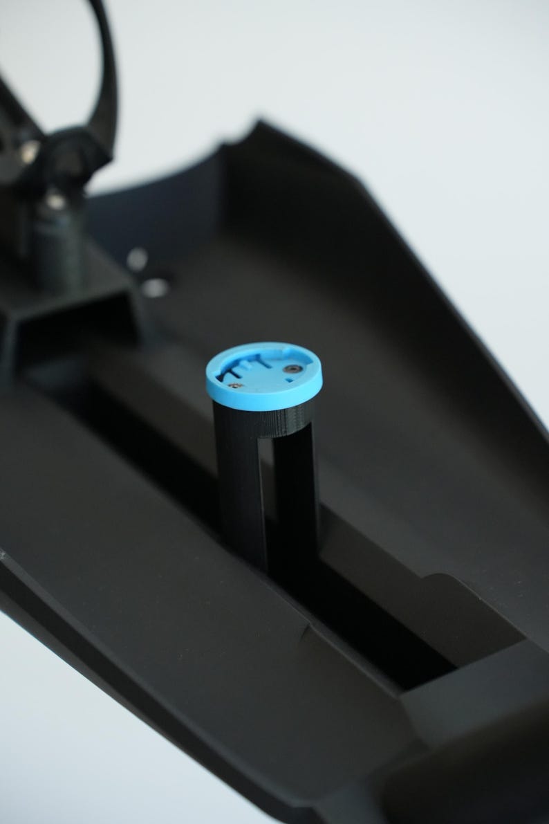 May include: A black plastic component with a light blue circular piece on top. The circular piece has a groove around the edge. The component is set against a white background.