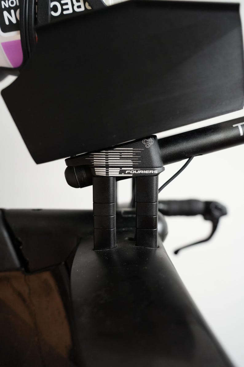 Pu&ograve; includere: Un attacco manubrio per bicicletta nero con un design grafico bianco e la scritta FOURIERS stampata sul lato. Il componente presenta due supporti cilindrici verticali che collegano il manubrio al telaio principale della bicicletta.