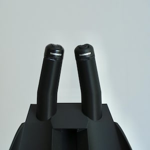 May include: Black bicycle handlebar grips with the brand name "Shimano" printed on the top. The grips are mounted on a black base. The image is taken against a white background.