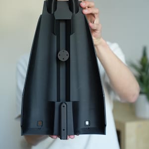 May include: A black, plastic component with two cylindrical nozzles and a central, elongated body. The component has a series of geometric cutouts and a circular attachment point. The object is held in front of a person.