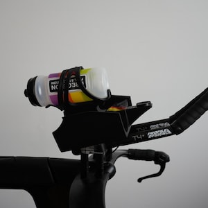Pu&ograve; includere: Un sistema di appendici aerodinamiche nero per bicicletta con portaborraccia montato e una borraccia bianca con grafiche colorate. Le appendici riportano la scritta T4+ Profile Design e includono nastro adesivo nero sulle impugnature e un supporto.